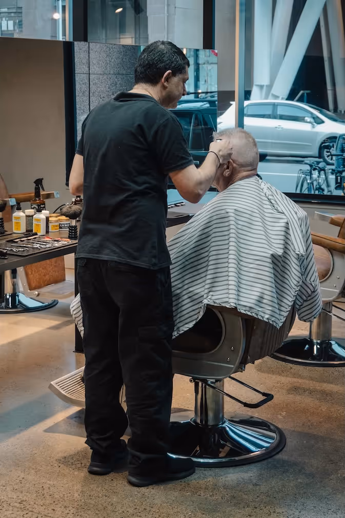 A barber carefully trimming a client's hair with scissors and a comb in a classic haircut.